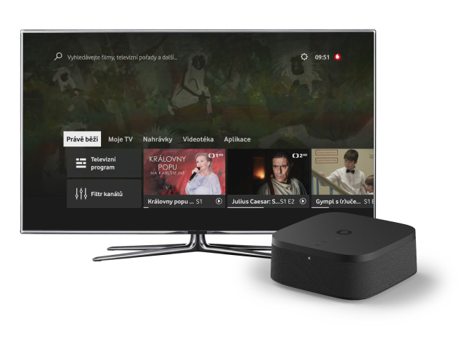 Televizor s moderním uživatelským rozhraním zobrazujícím nabídku televizních programů a aplikací, vedle něj černý set-top box Vodafone TV Play