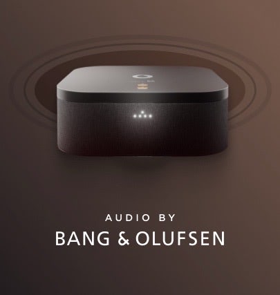 Černý set-top box na hnědém pozadí s logem Bang & Olufsen a textem „AUDIO BY BANG & OLUFSEN“ pod ním. Kolem zařízení jsou kruhové zvukové vlny naznačující šíření zvuku.